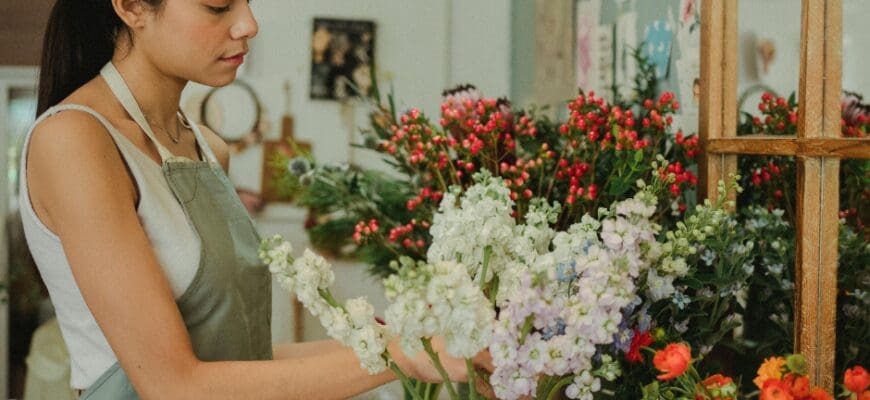 A Woman Arranging Multiple Large Bouquets of Flowers in vases on a Shelf